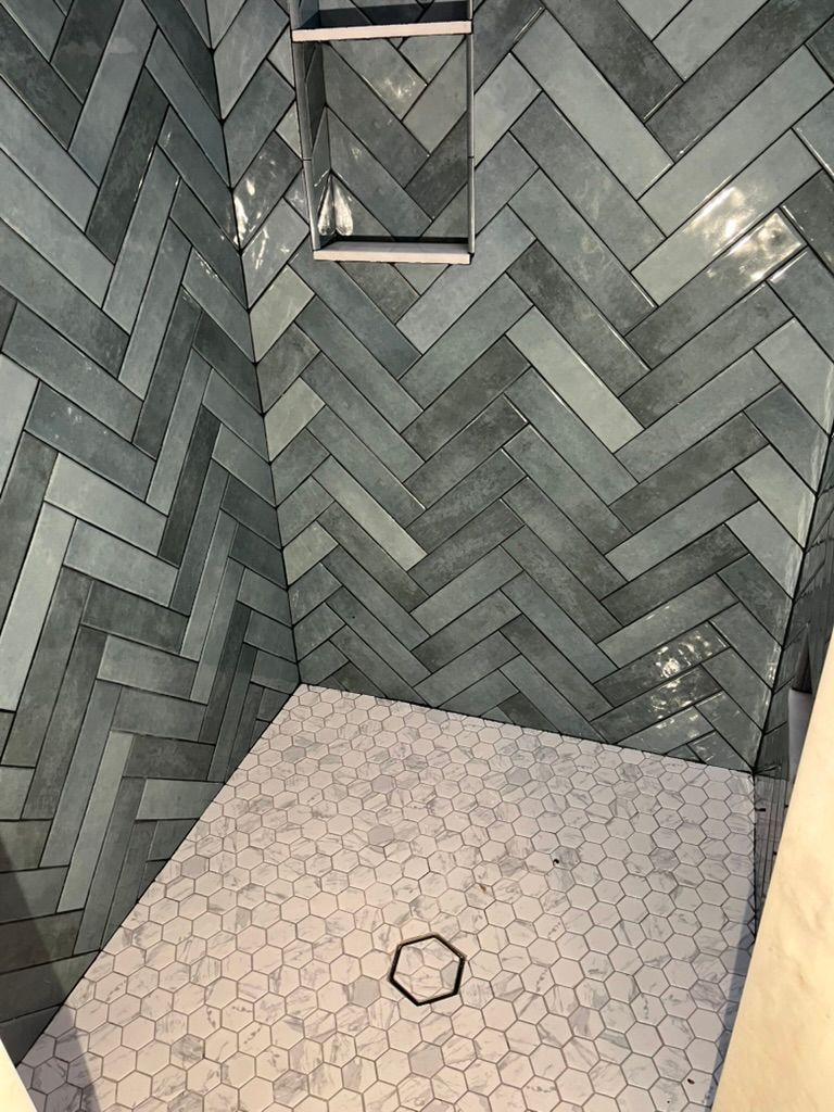 Shower with blue herringbone tile walls and small, light-colored mosaic floor.
