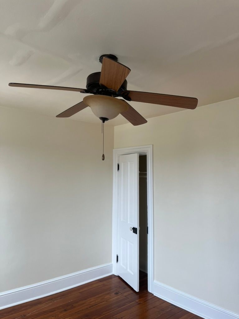 Ceiling fan with wooden blades in a room with a closed white door.