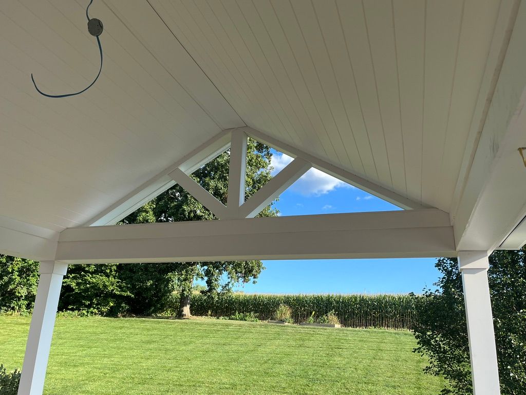 White-painted porch with triangle gable, overlooking a green lawn and blue sky.
