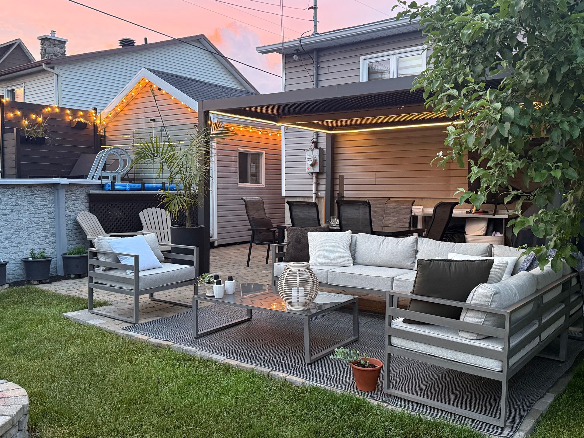 Terrasse arrière avec mobilier moderne, pergola et guirlandes lumineuses au crépuscule.