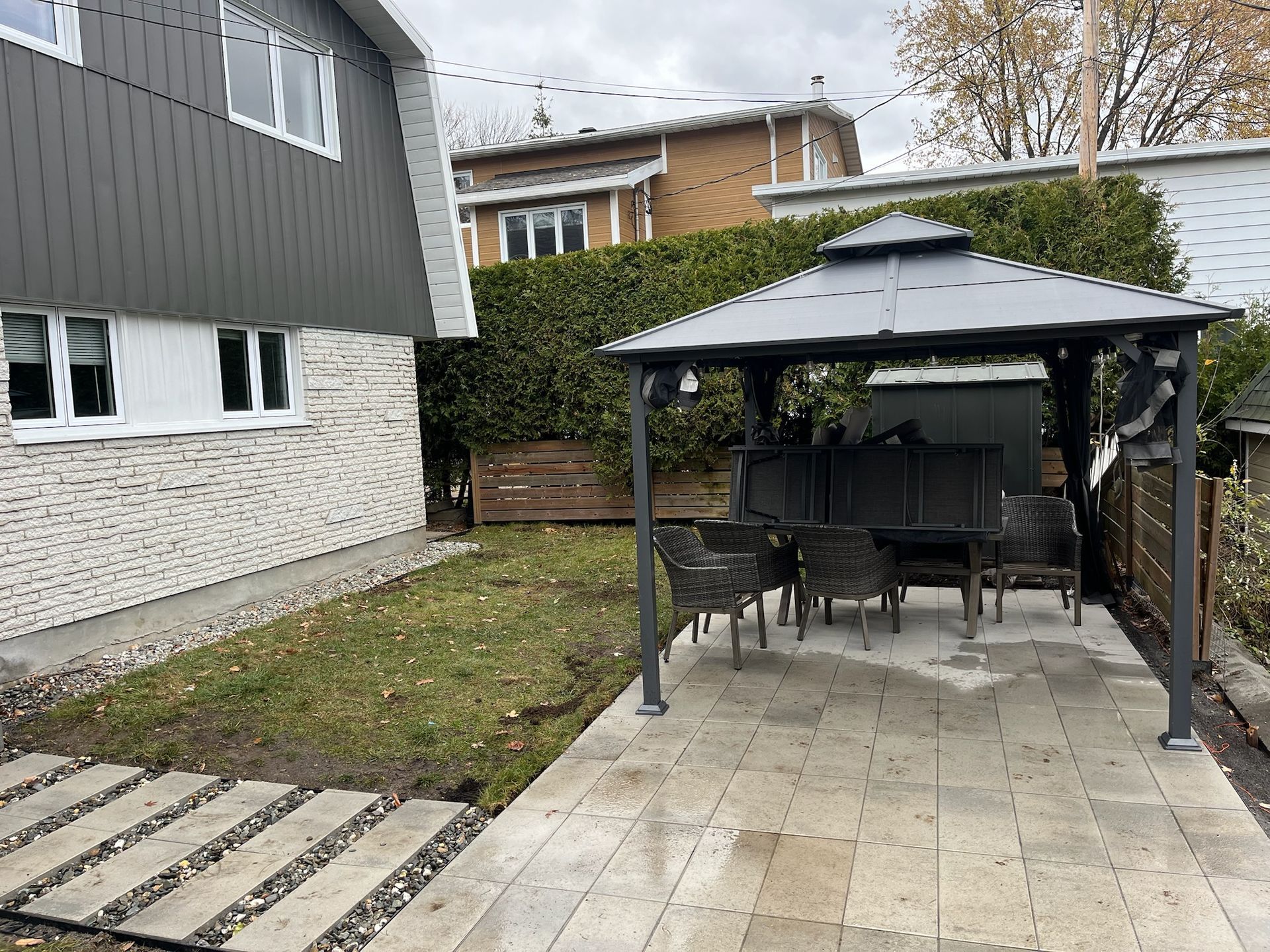 Cour arrière avec patio et gazebo, ensemble de salle à manger et maison avec revêtement gris et briques.