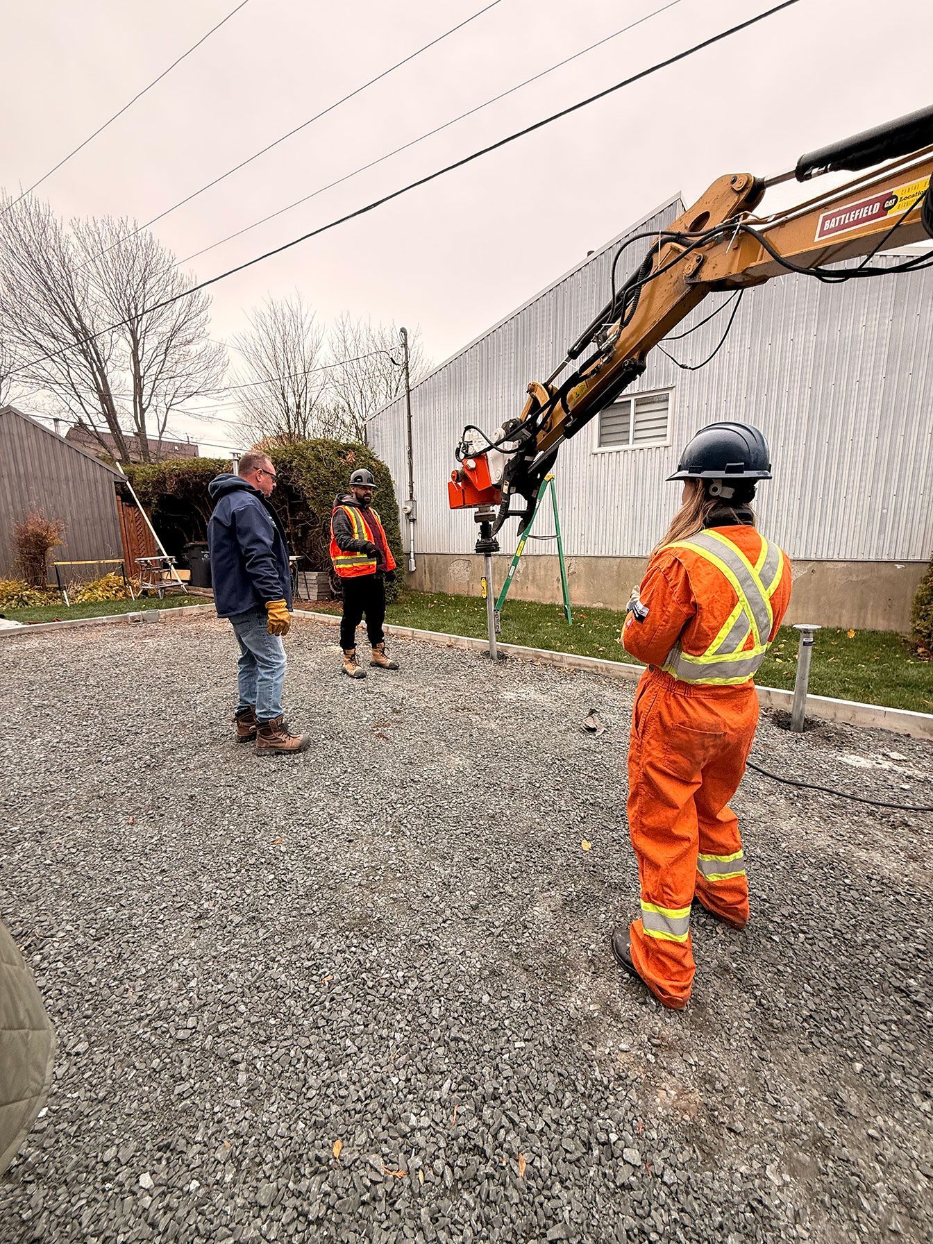 Des ouvriers équipés de tenues de sécurité manœuvrent des machines à proximité de lignes électriques et d'un bâtiment.