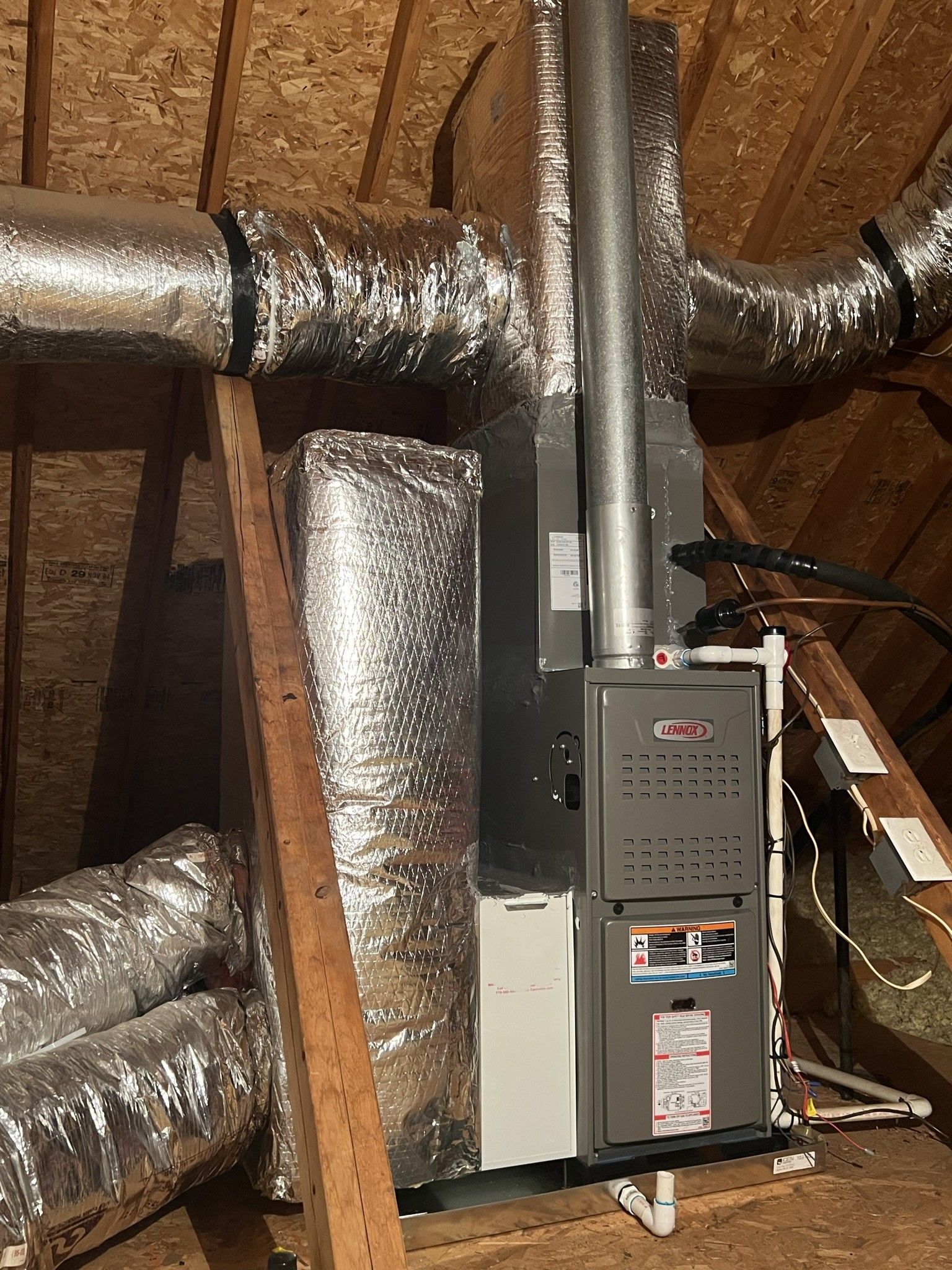 Furnace and ductwork in an attic, with metallic insulation and wooden supports.