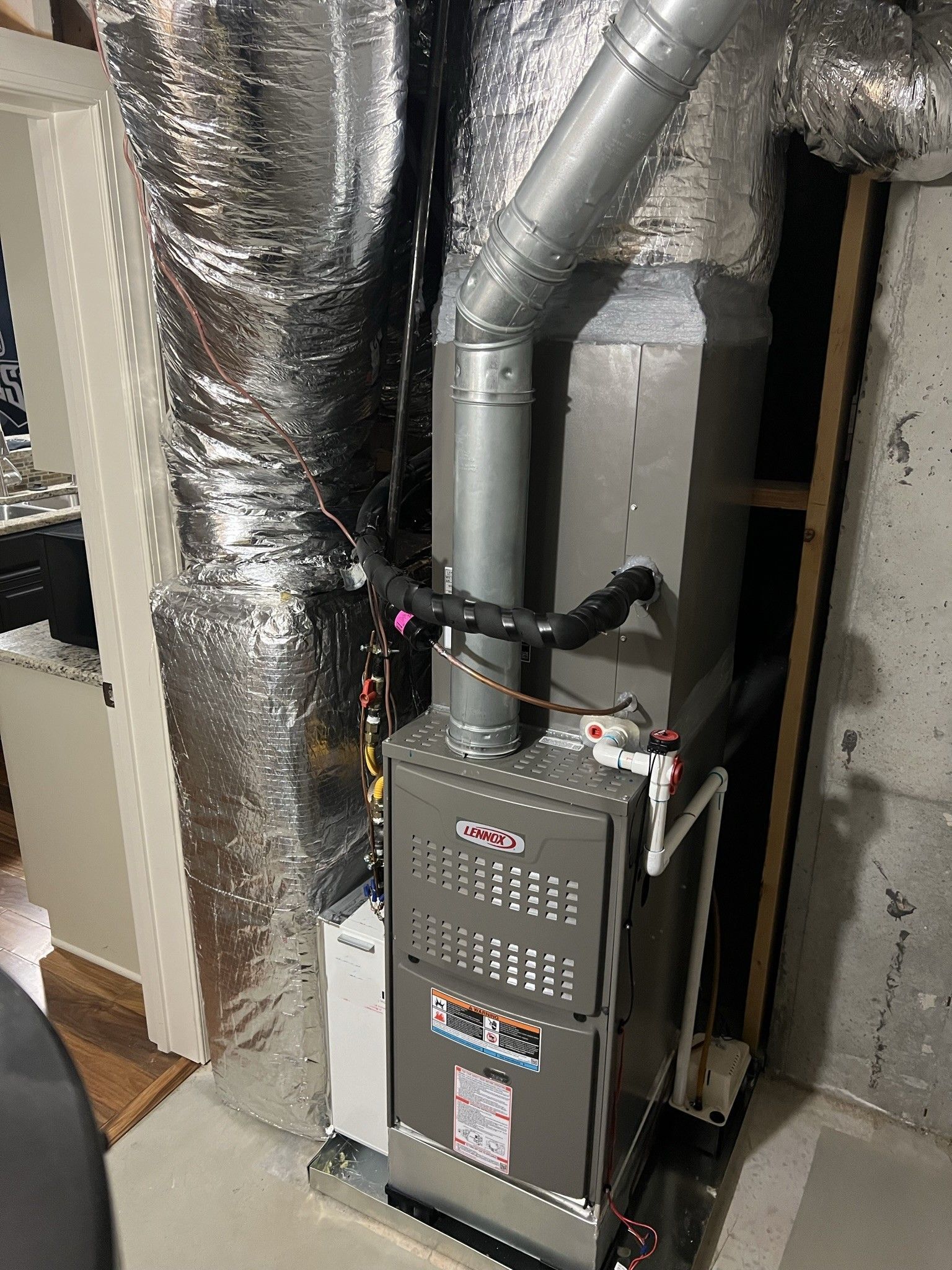 Furnace in a basement. Ductwork and flue pipe visible. Gray, silver, and black.