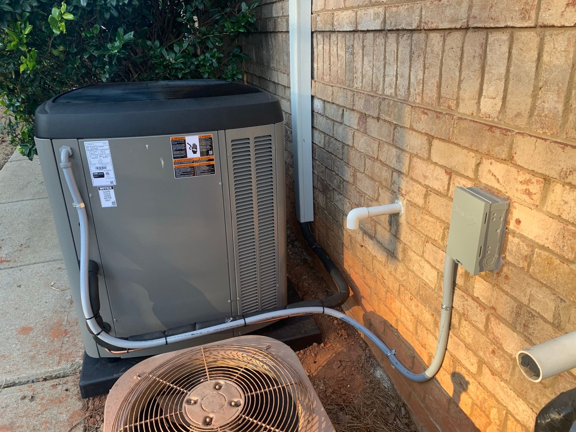 Air conditioning unit beside brick wall with electrical box. Grey and brown tones.