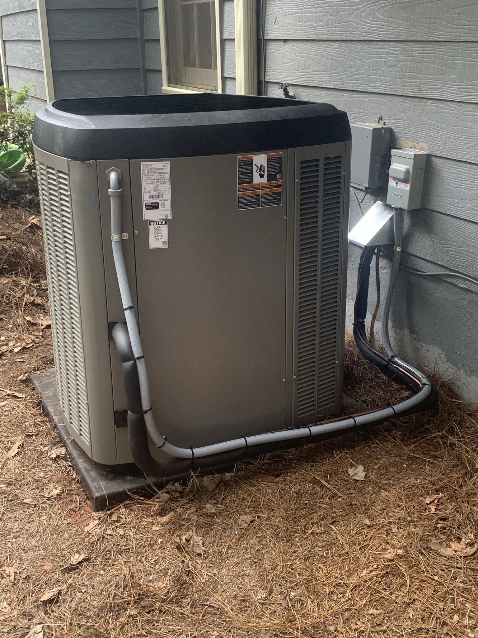 Central air conditioning unit outside on a gravel bed, against a blue house wall.