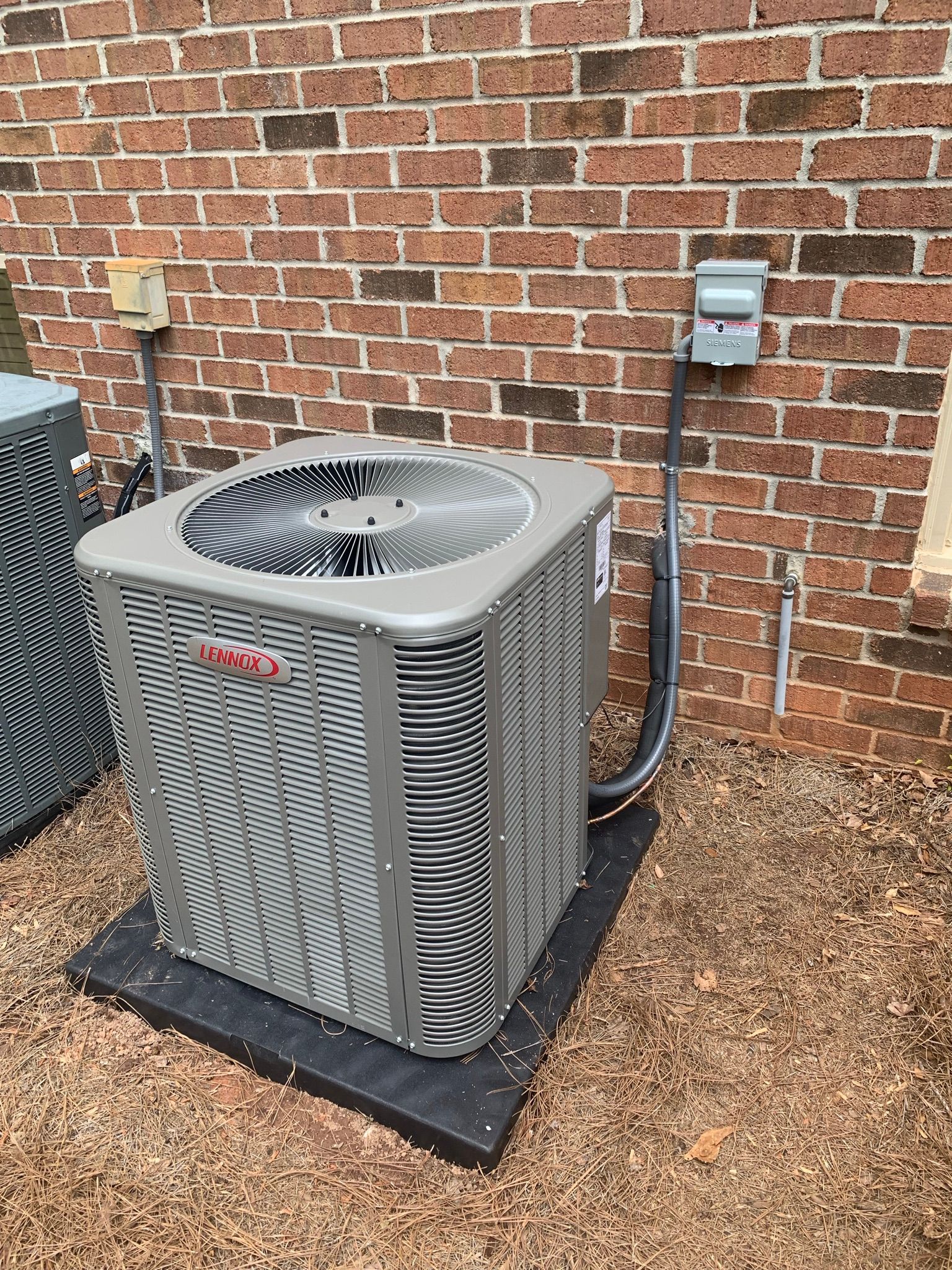 Air conditioner unit outside brick building. Gray metal, black base, power boxes.