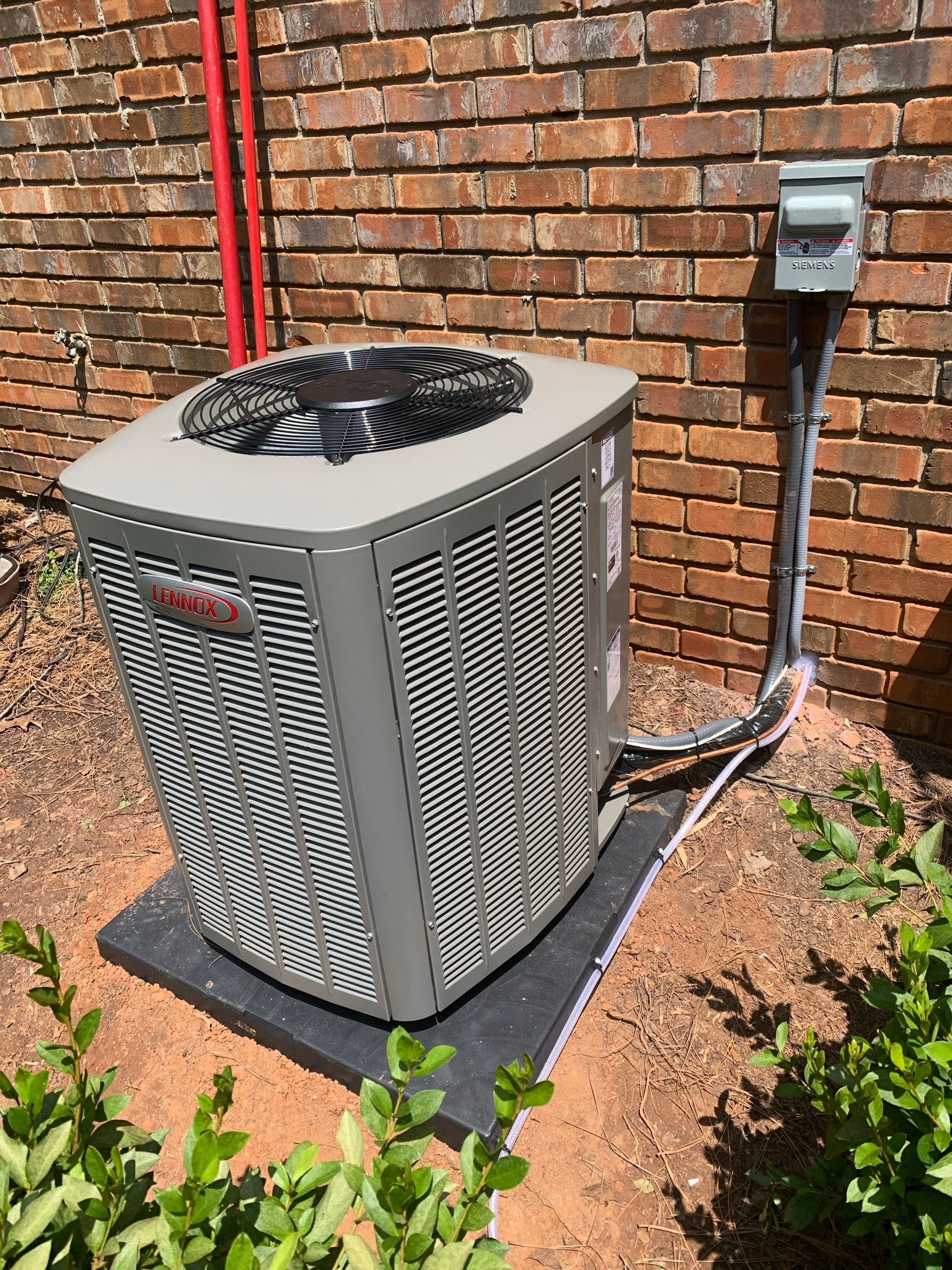 Air conditioning unit against a brick wall. Gray, modern unit on a black base; electrical box on wall.