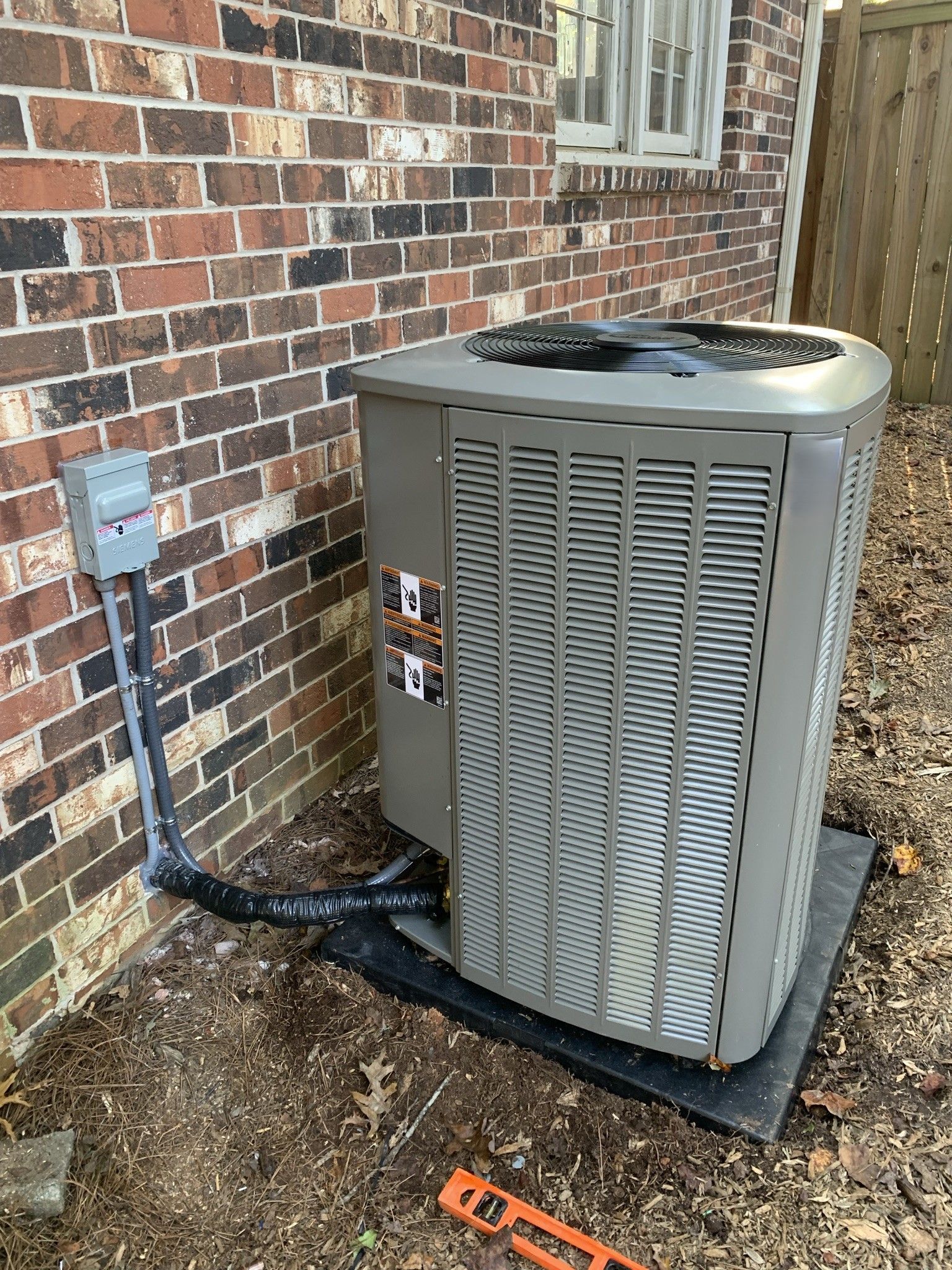 HVAC unit next to a brick wall with electrical connections and a leveler.
