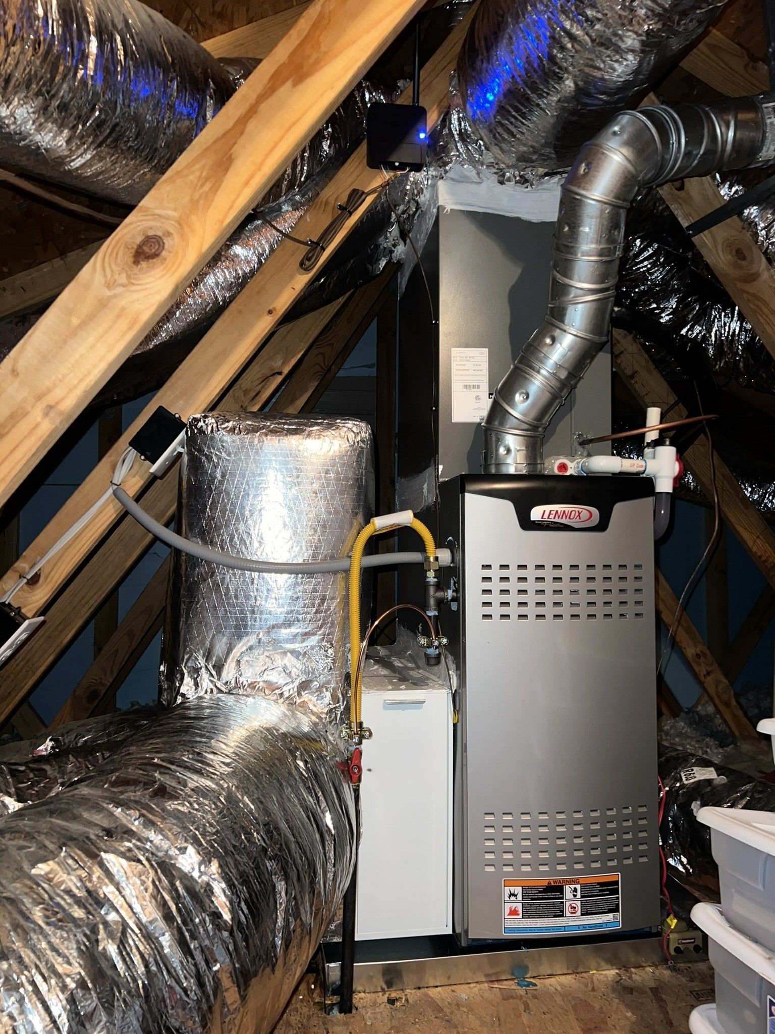 HVAC system in attic with silver ductwork, gray furnace, and white water heater. Wooden beams support the structure.