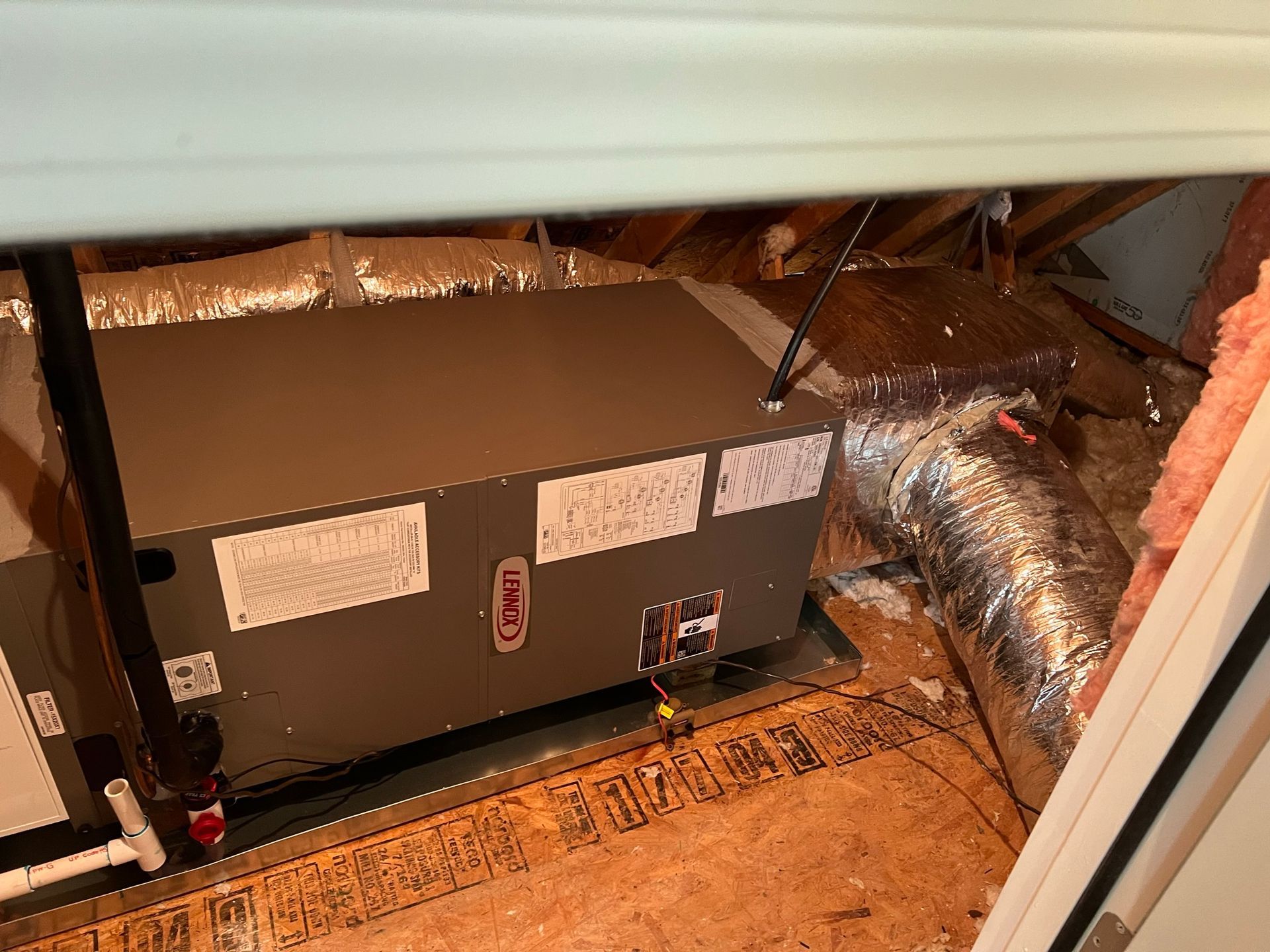 A gray HVAC unit in an attic with insulated ductwork and exposed wooden beams.