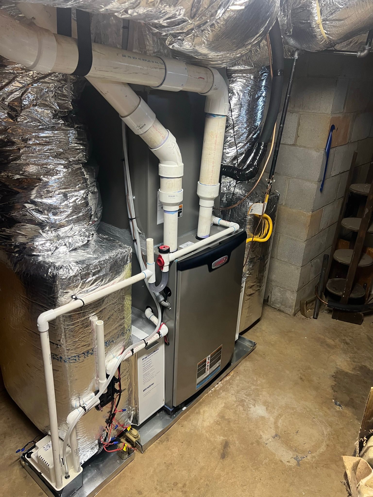 Furnace unit with white pipes and silver ductwork in a basement setting.