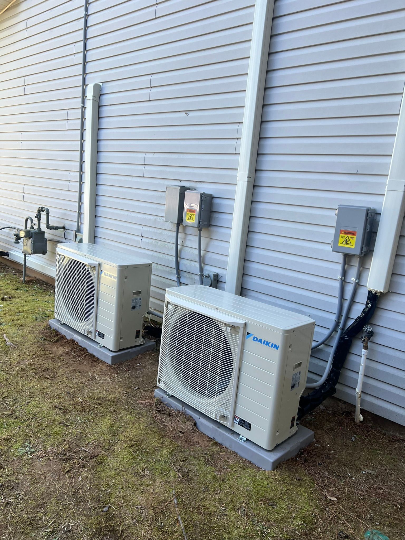 Two outdoor heat pump units mounted on concrete pads beside a building with gray siding.