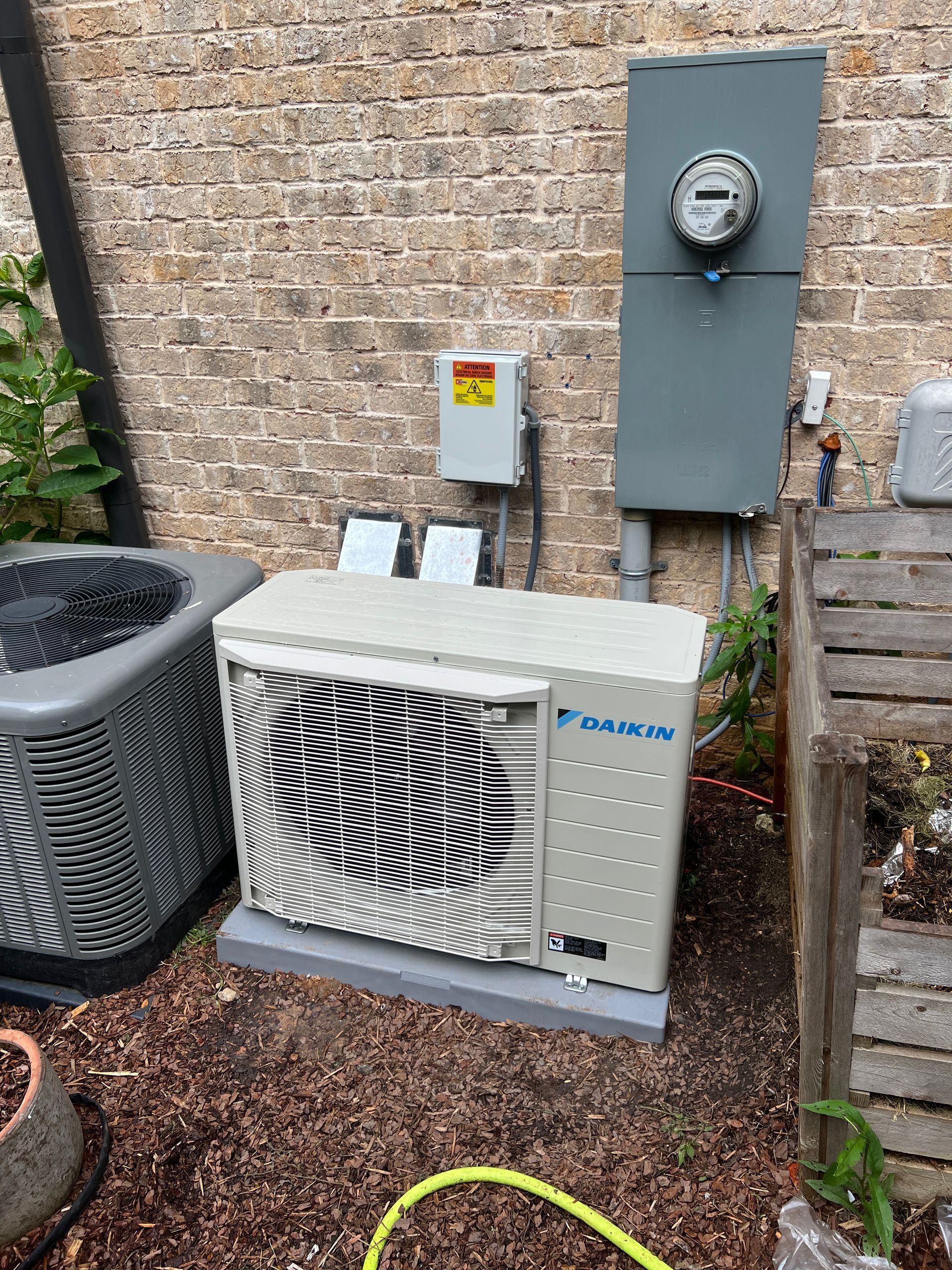 Daikin heat pump unit next to an electrical box on a brick wall, outdoors.