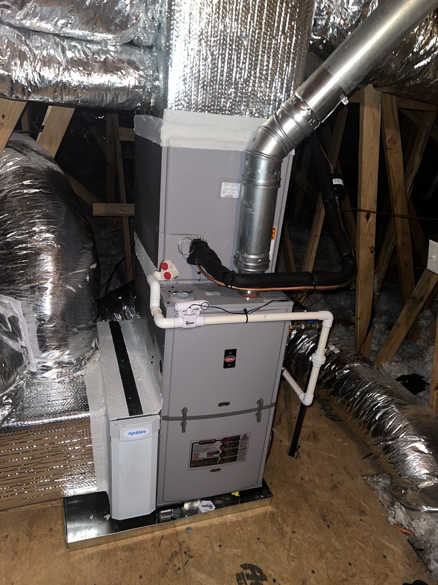 HVAC unit in an attic. Ductwork is insulated silver. Unit is gray and white.