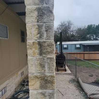 Stone porch column beside a beige house, with a gravel yard, fenced patio, and grill in the background.