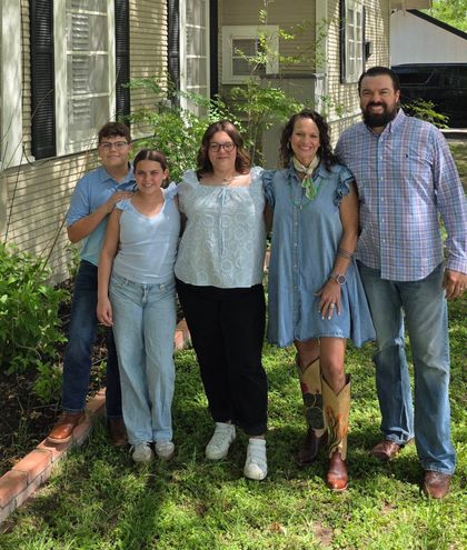 Five people standing together outdoors in front of a house, smiling in casual clothes.
