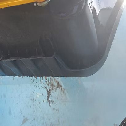 Close-up of a black plastic container corner over a light blue surface with dirt splatter.