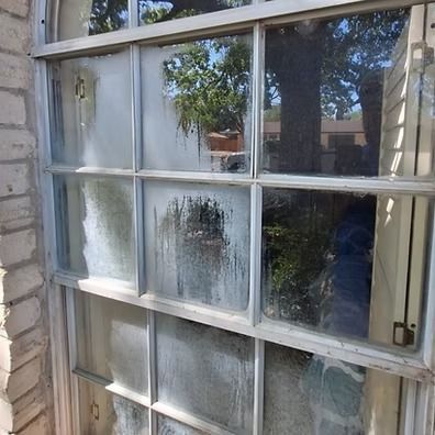 Old window with frosted, dirty glass panes reflecting trees and a house.