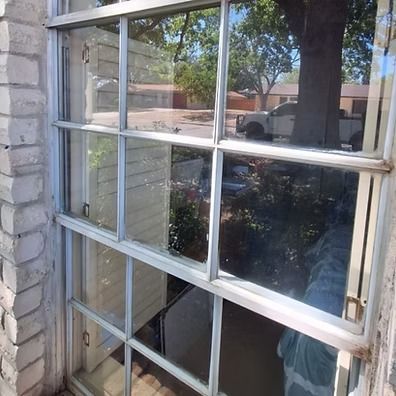 Broken window panes on a house, with reflections of trees and a parked car outside