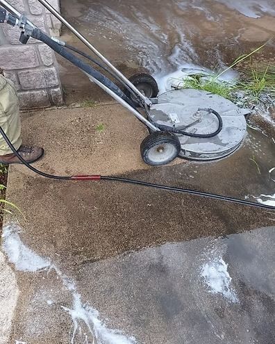 Person using a pressure washer on a wet concrete surface near a house wall.