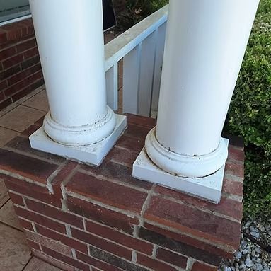Two white porch columns mounted on a brick base beside a railing and walkway