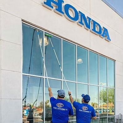 Two workers in blue shirts install window film on a Honda dealership facade