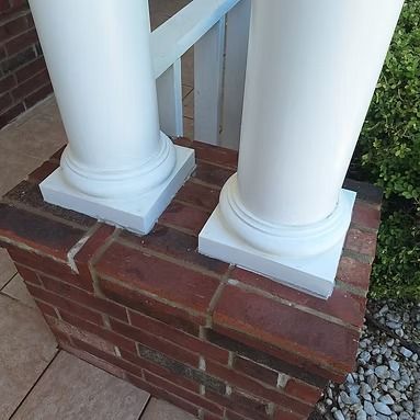 White porch columns on a red brick base beside a brick wall and shrubbery