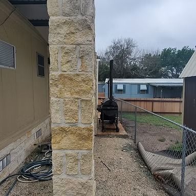 Stone pillar beside a gravel yard with a black smoker grill and chain-link fence in a backyard