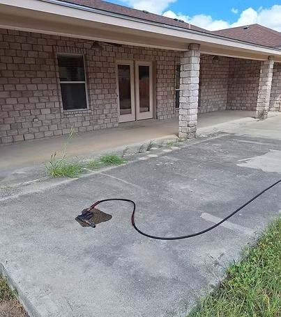 A black cable snakes across a driveway in front of a brick house with a covered porch.
