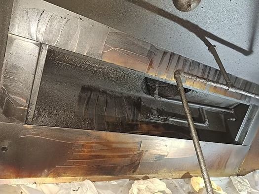 A greasy metal oven vent or duct opening with a rod inserted into the dark interior.