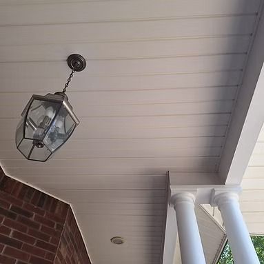 Hanging glass porch lantern under a white ceiling beside a brick wall and white columns