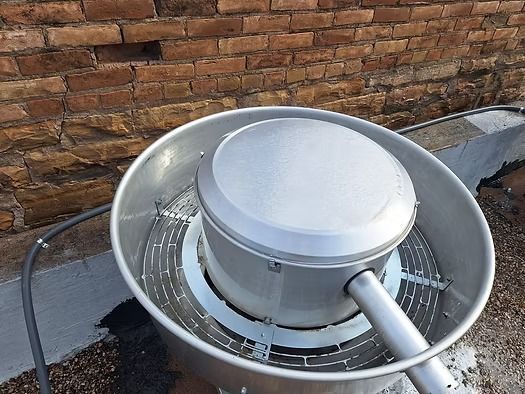 Metal rooftop satellite dish beside a brick wall, with a white circular receiver and arm.