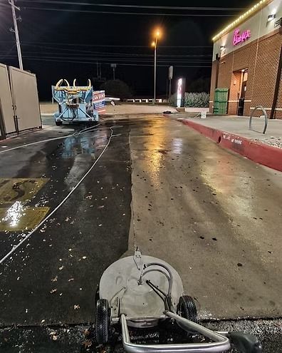 Wet parking lot at night with a pressure washer in the foreground and a building on the right.