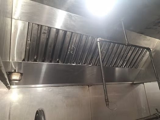 Stainless steel commercial kitchen vent hood and grease filters with a bright ceiling light above.