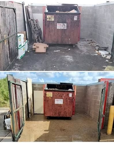 Red dumpster in a narrow alley beside concrete walls and scattered debris.