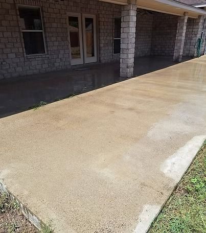 Concrete driveway beside a stone house, with a covered porch and grassy edge.