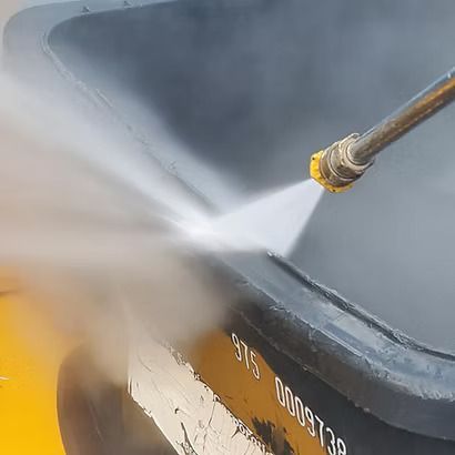 High-pressure water spraying the side of a black dumpster, cleaning off grime and paint.
