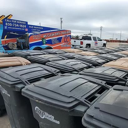 Rows of black trash bins in a lot beside a colorful tow truck under a cloudy sky.