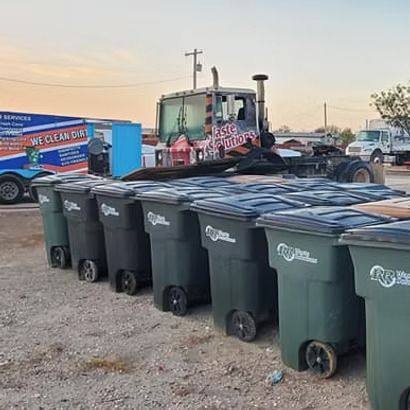 Row of trash bins in a gravel lot beside a truck and trailer at dusk
