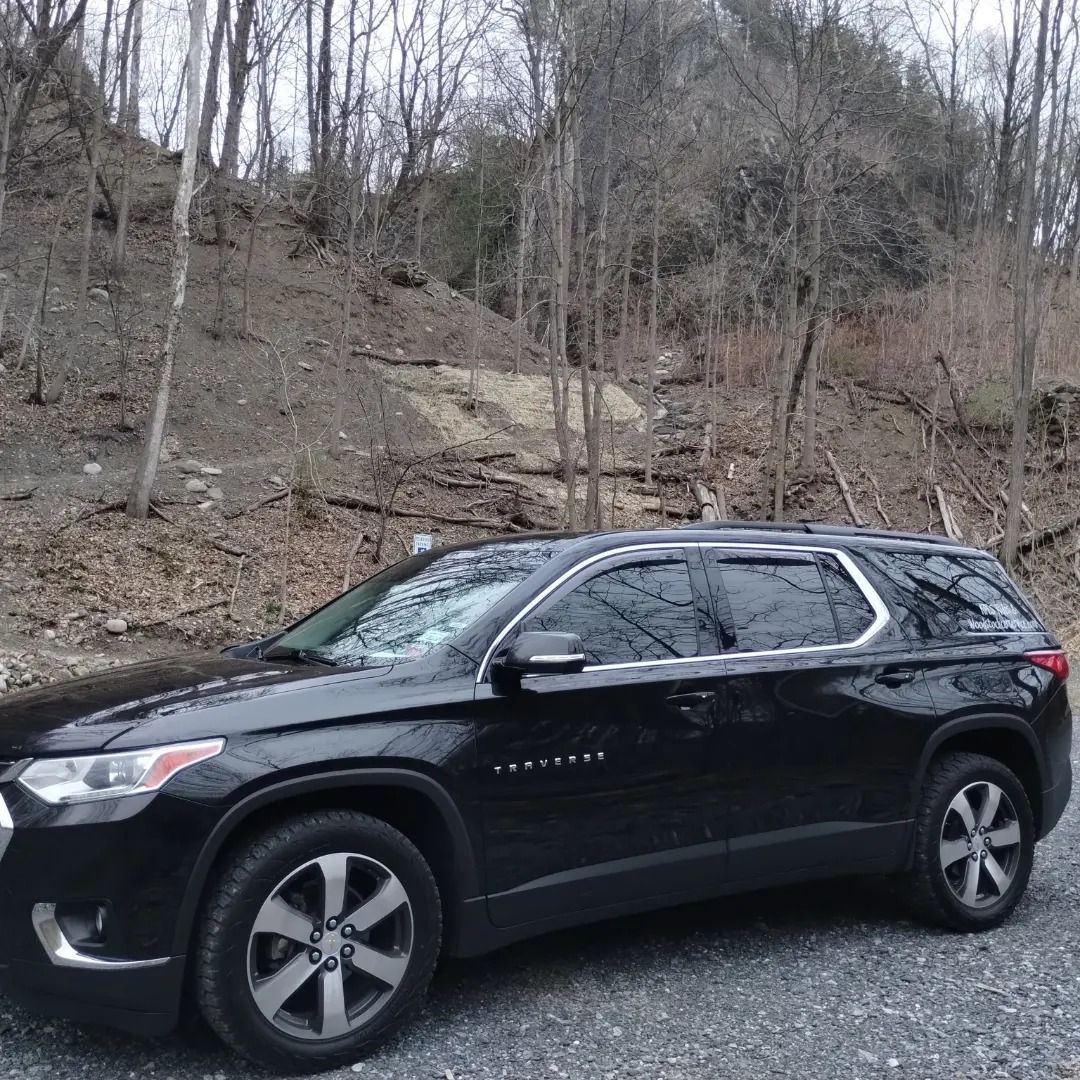 A black suv is parked in a gravel lot in front of a forest.