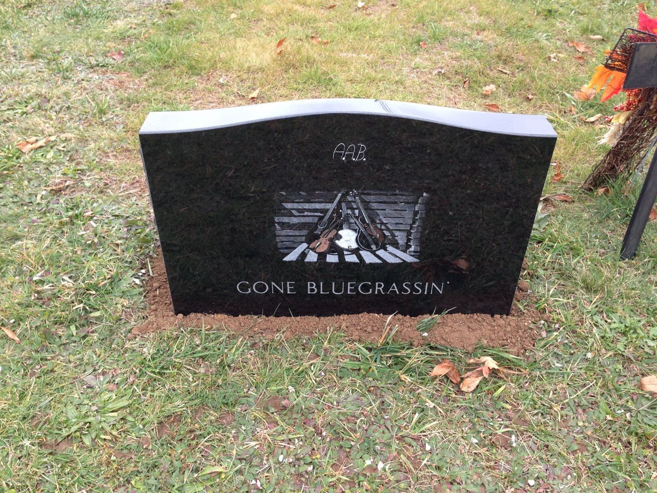 A black gravestone with the words gone bluegrassin on it