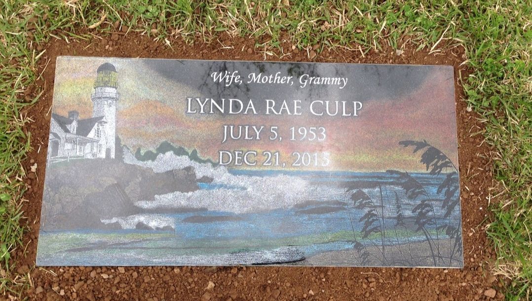 A gravestone with a lighthouse on it is in the grass.