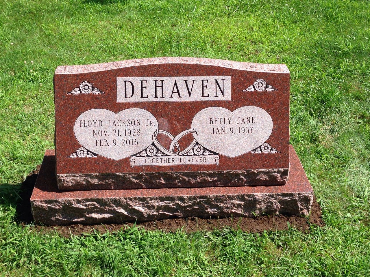 A red gravestone with two hearts on it in a cemetery.