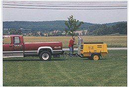 A red truck is towing a yellow trailer in a field.