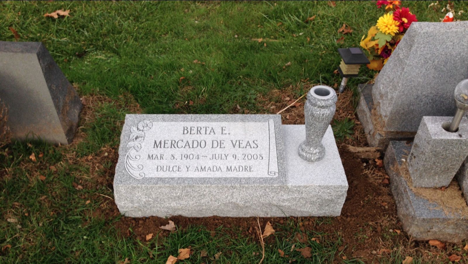 A gravestone with a vase on top of it in a cemetery.