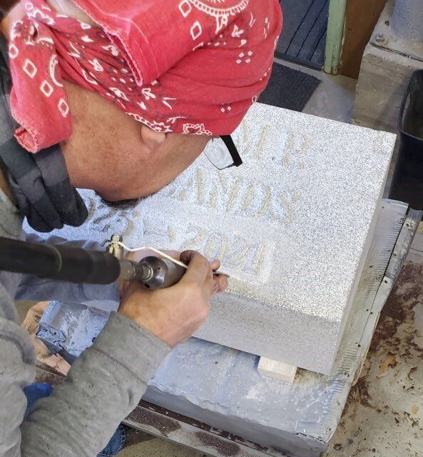 A man wearing a red bandana is carving a stone