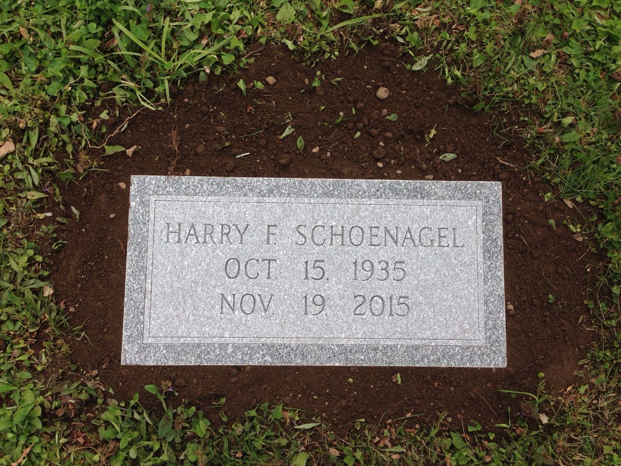 A gravestone for harry e schoenagel is in the grass
