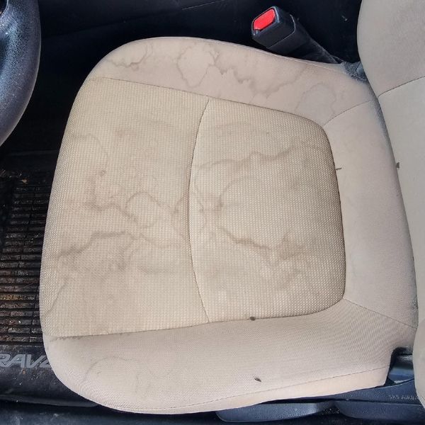 A beige car seat covered in large, irregular brown water stains and spots.