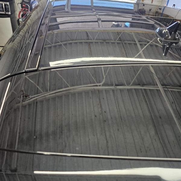 The reflective, dark roof of a vehicle, showing a distorted view of a white, beamed ceiling structure overhead.
